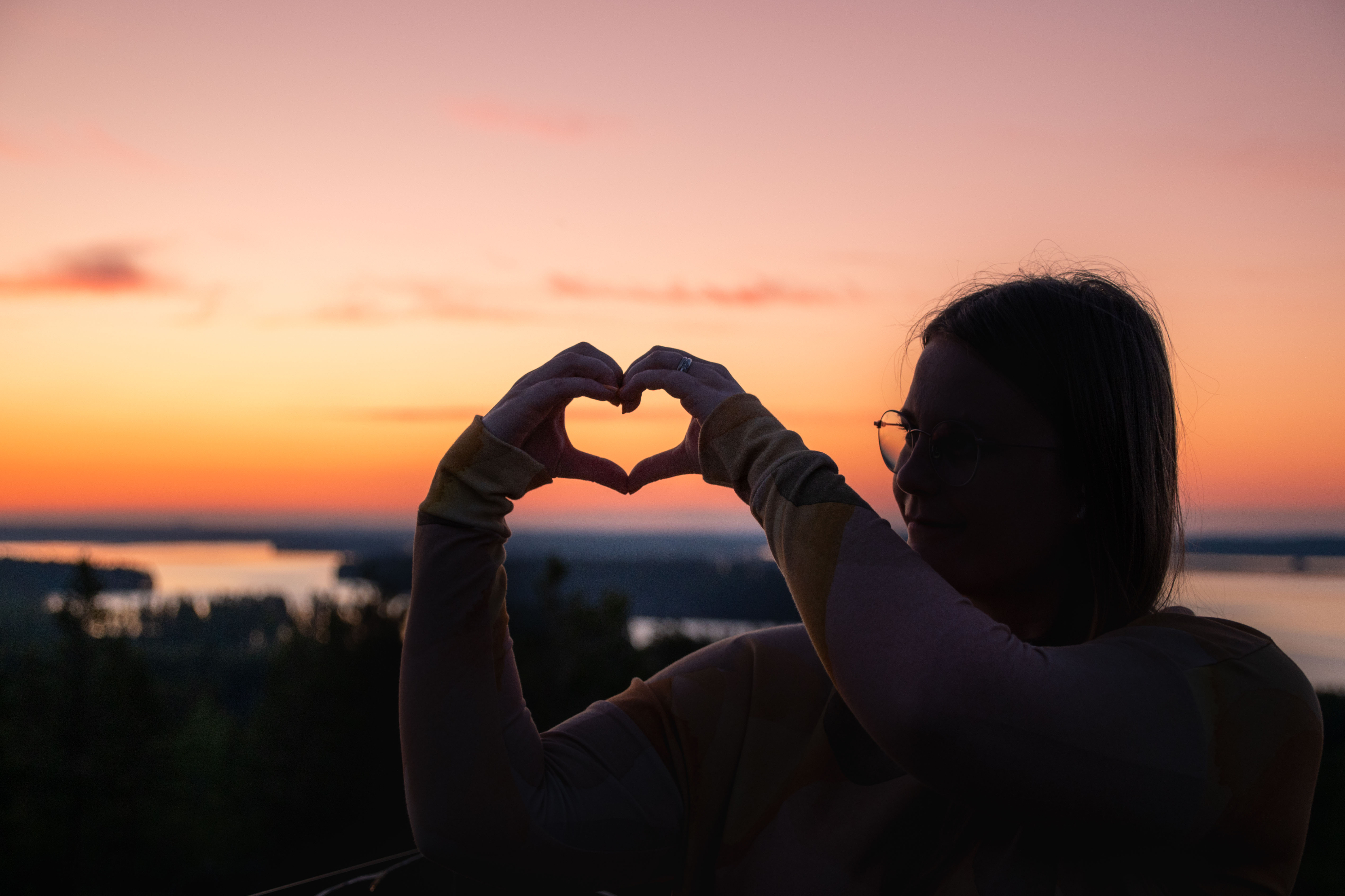 Nainen auringonlaskussa muodostaa käsillä sydämen.